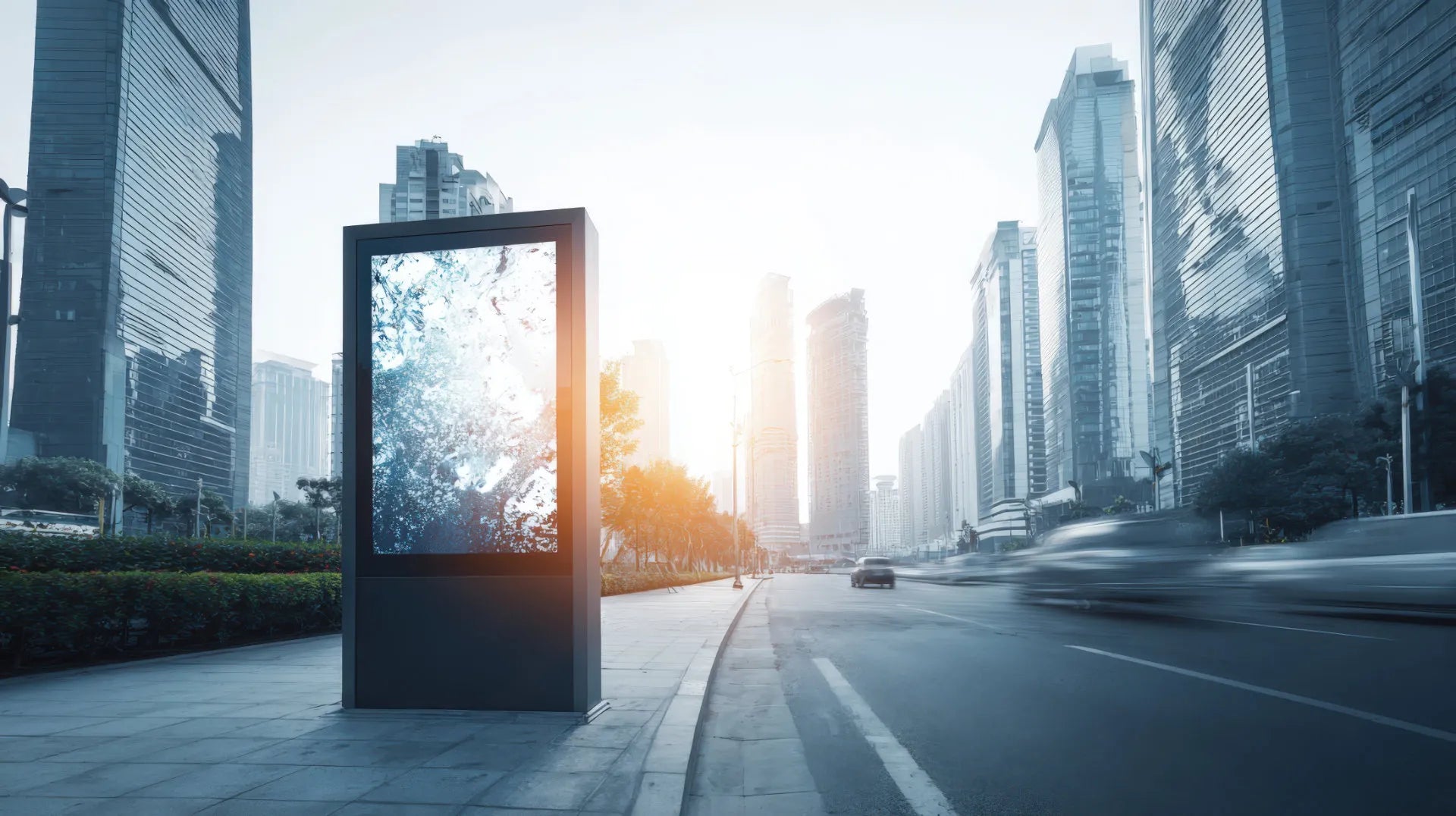 A large digital billboard on a city sidewalk beside a busy road with skyscrapers behind it.